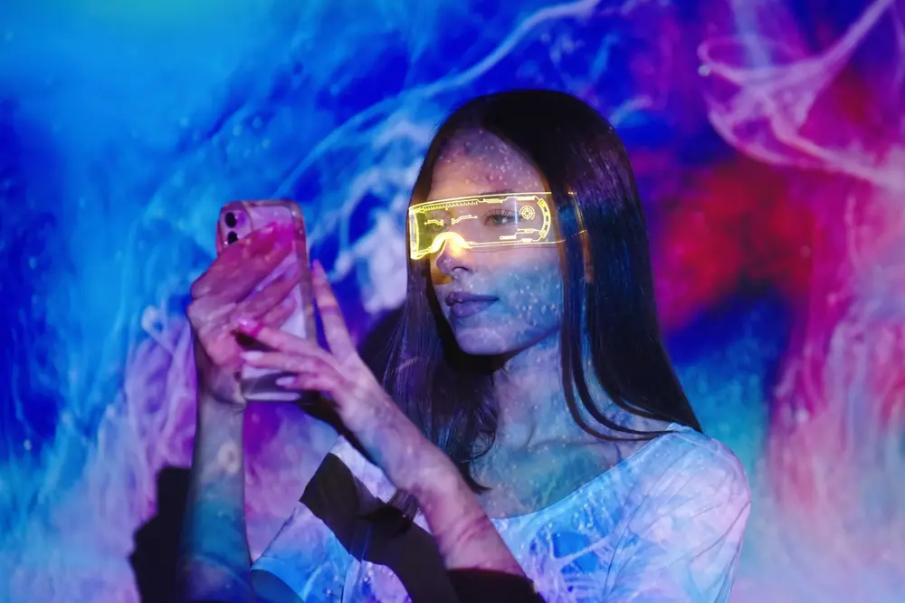 Foto de uma mulher, usando oculos futuristas, enquanto segura e mexe em um smartphone